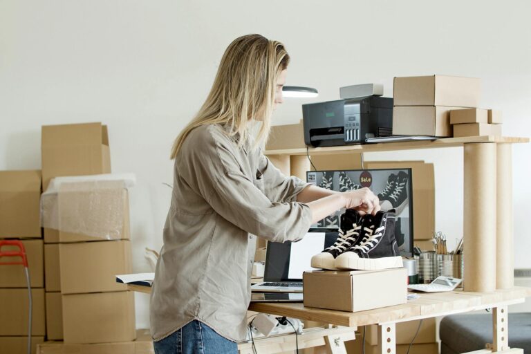 A woman packs sneakers in a box at her e-commerce workspace, surrounded by packing materials.